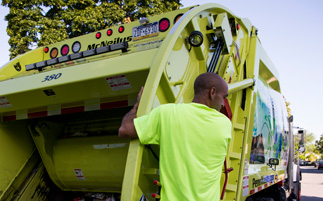A Penn Waste employee on the back of a recycling truck.: Click to open Facility Tour video